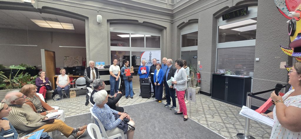 Group of adults standing in a gray atrium as they receive or present awards to a seated audience.